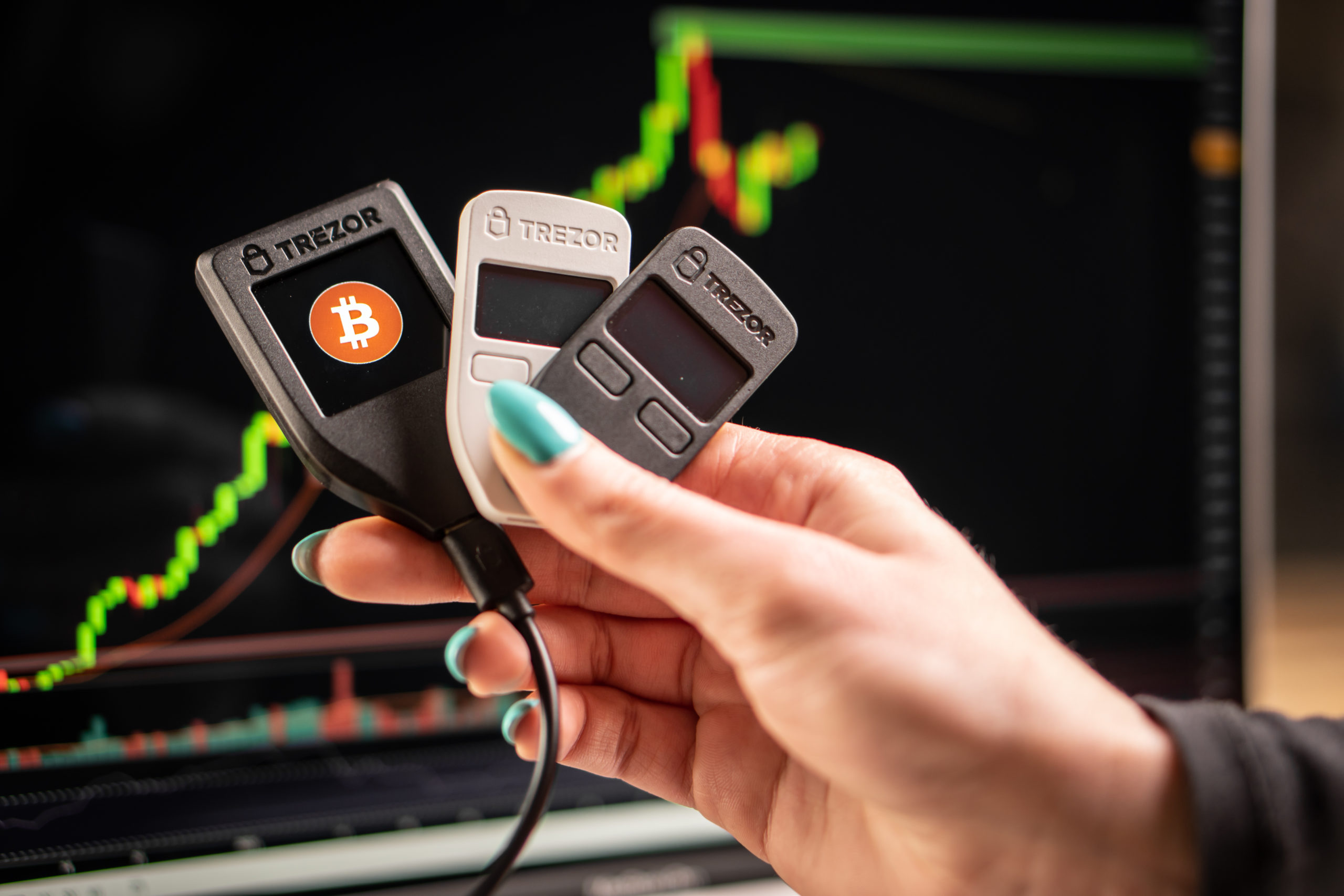 Trezor hardware wallets held in hand in front of graph