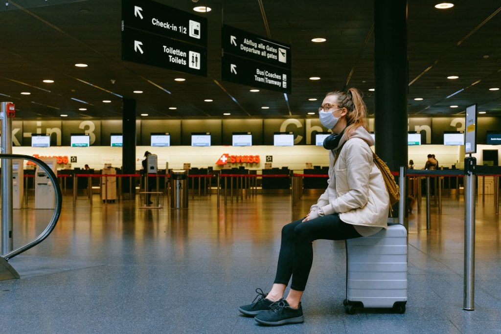 Una mujer con mascarilla sentada sobre su maleta en un aeropuerto