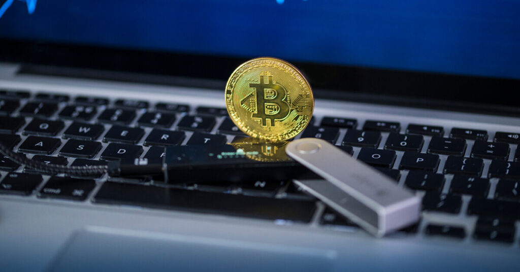 A gold Bitcoin and a ledger hardware wallet placed on a laptop keyboard