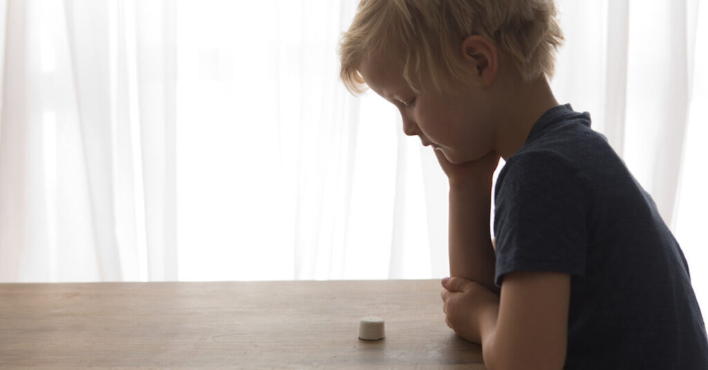 A kid looking at a marshmallow on a table