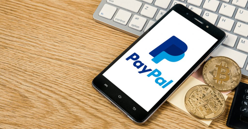 Logo de PayPal en un teléfono móvil sobre un escritorio con bitcoins al lado