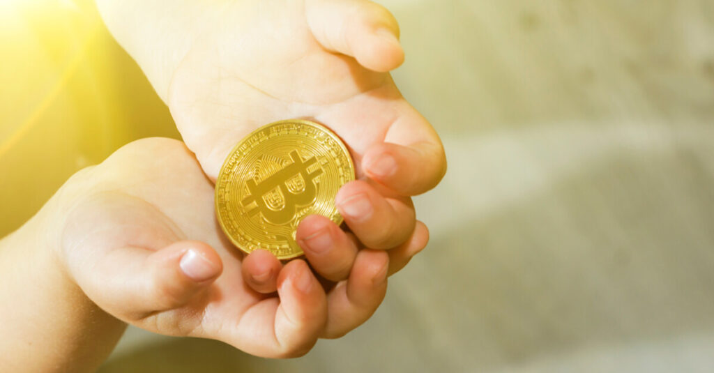 A Bitcoin gold coin being holded by a pair of hands.