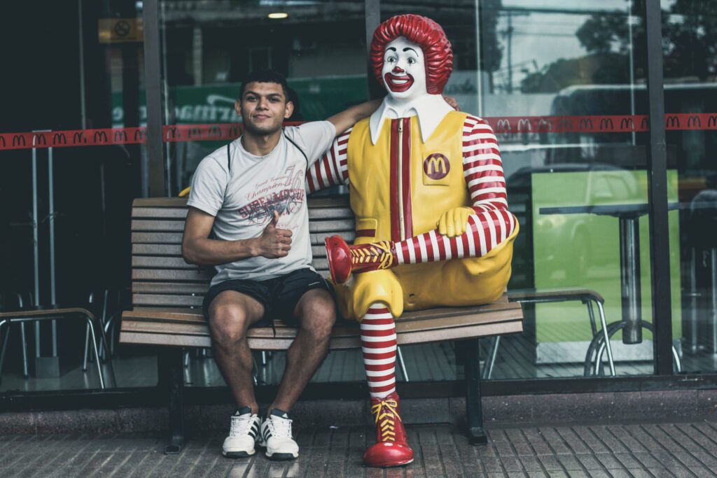 Man sitting next to a Ronald McDonald statue