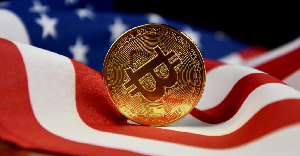 A golden Bitcoin coin propped upright on a flag of the U.S.