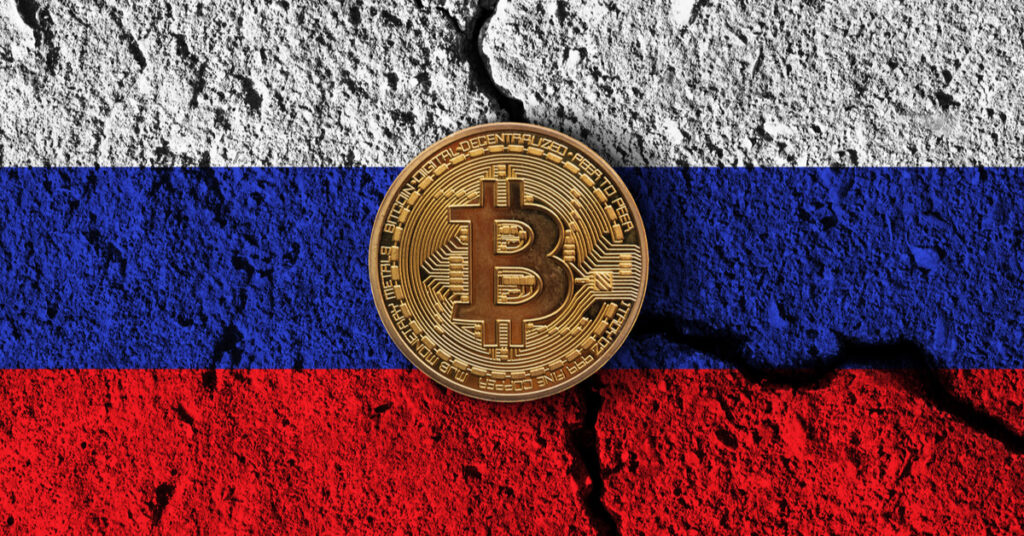 Golden bitcoin coin in front of a cracked Russia flag