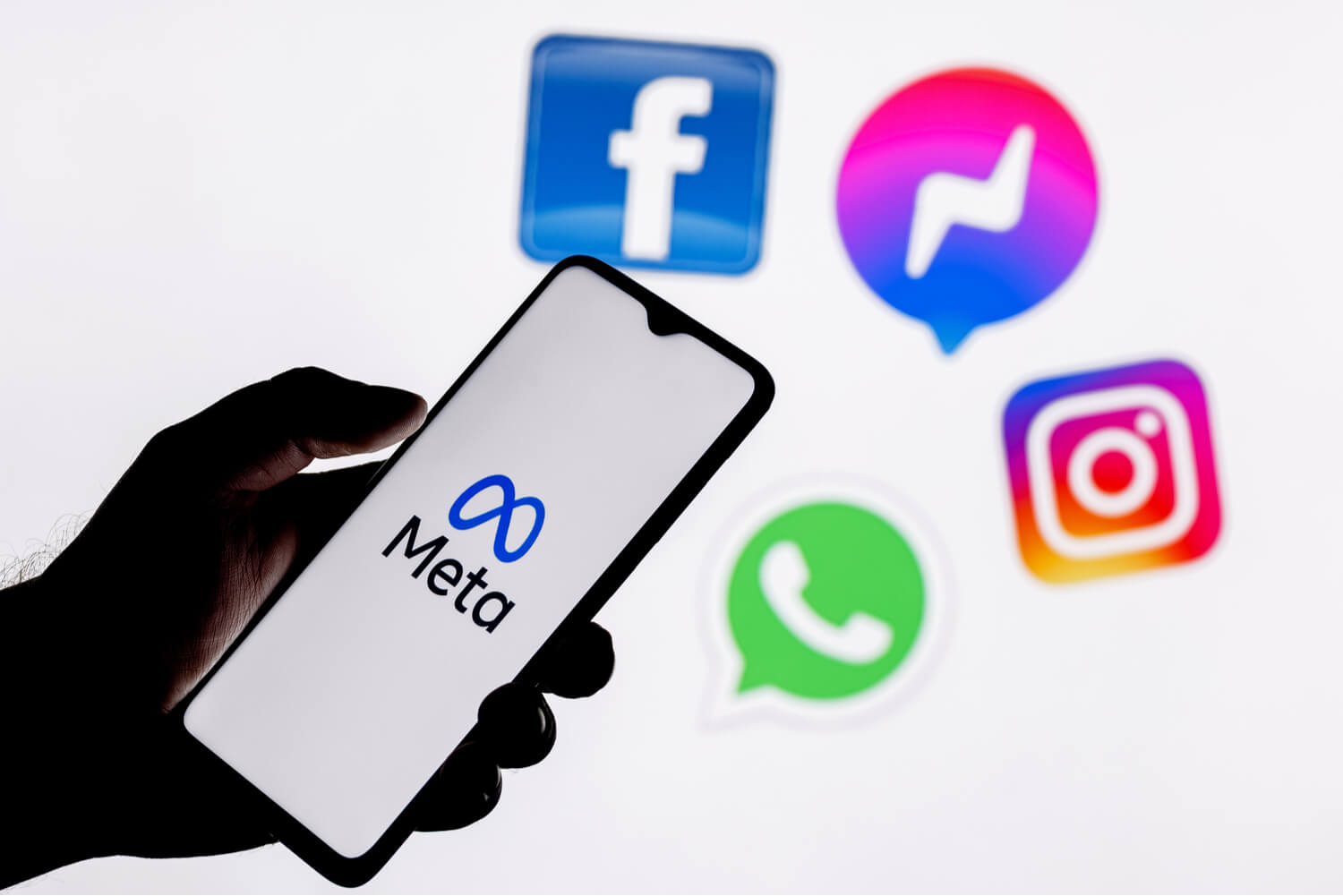 Meta symbol on a smartphone in front of the social media logos of Facebook, Instagram, WhatsApp, and Messenger