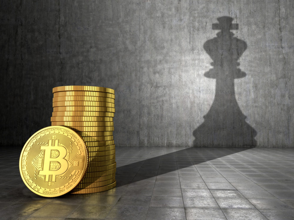 A stack of Bitcoins at the foreground with a shadow showing the king in chess projected onto a wall