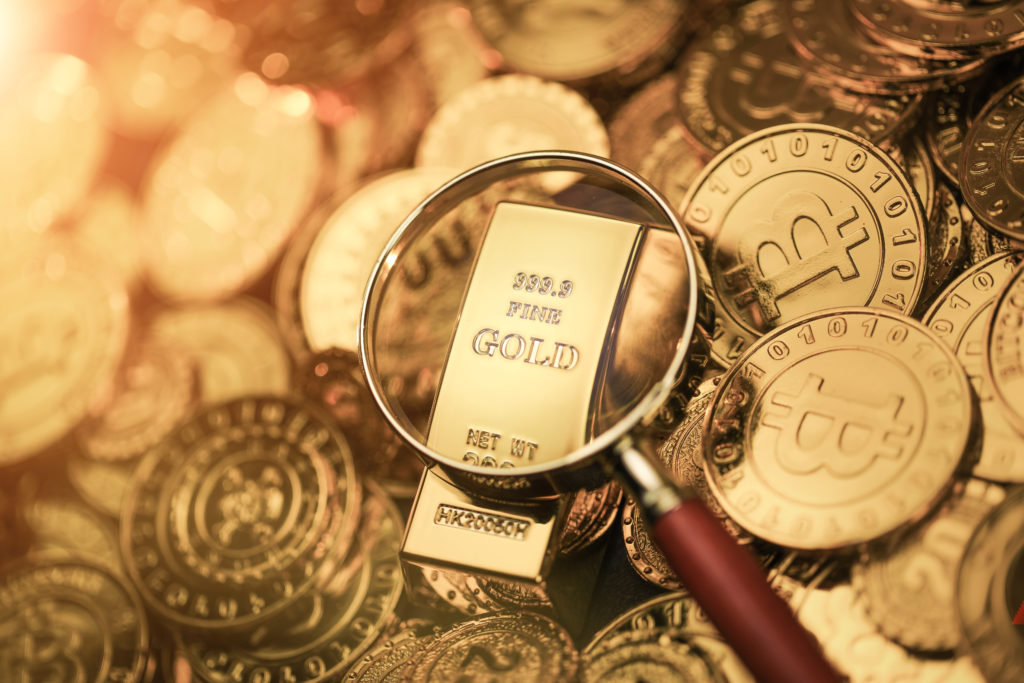 A pile of several Bitcoins, represented in physical gold coin form, with a magnifying glass looking at a gold bar in the middle of the pile.