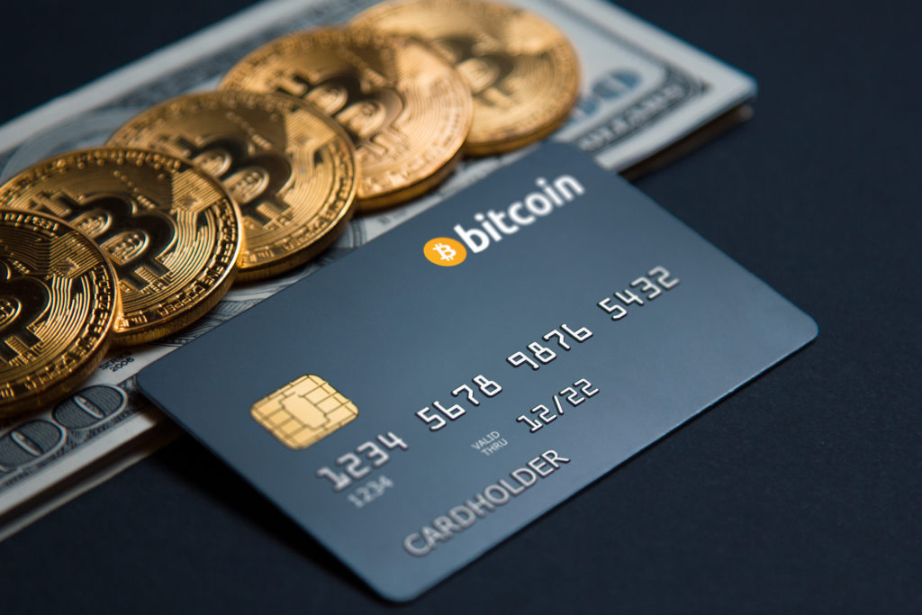 A bitcoin credit card with Bitcoins next to it on top of 100 dollar bills