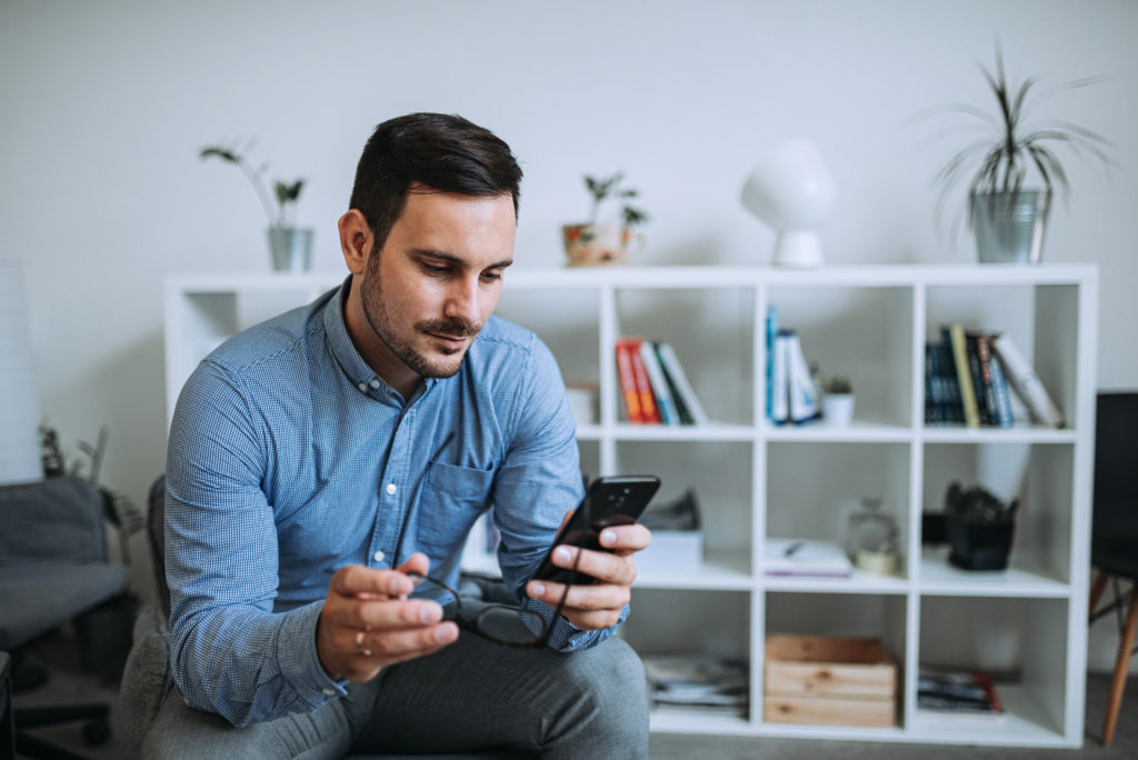 Hombre mirando su teléfono móvil y sujetando unas gafas 