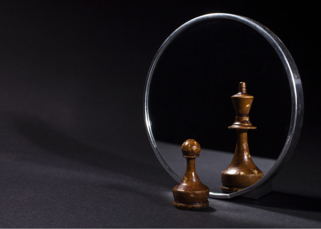 A chess pawn in front of a mirror with chess king reflected in the mirror