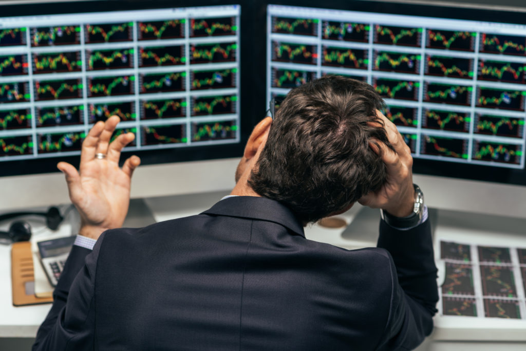 Man looking stressed in from of stock price screens