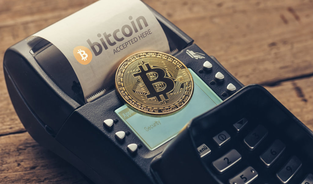 A Bitcoin, represented as a physical gold coin, on top of a card machine with a receipt saying 'Bitcoin accepted here'.