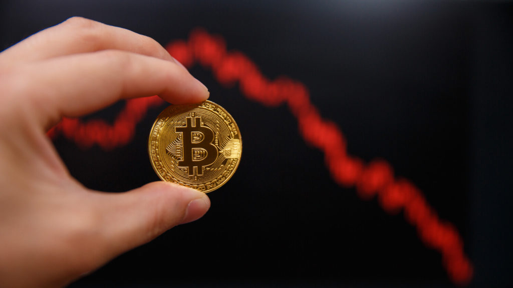 Bitcoin coin in front of declining line chart