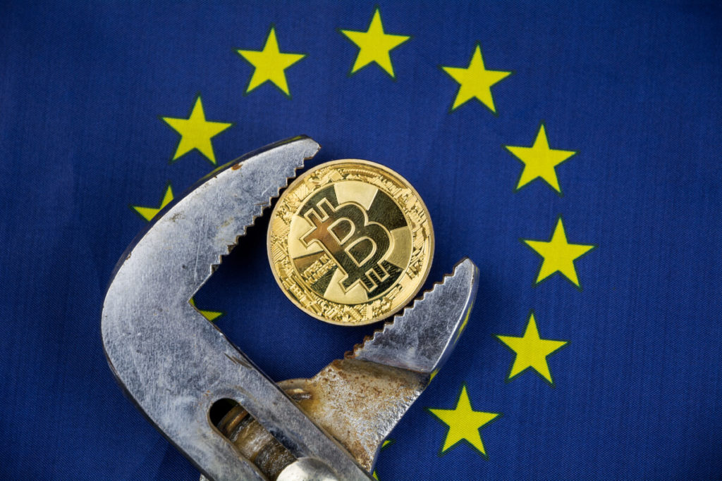 Golden Bitcoin within a clamp in front of a European Union flag 
