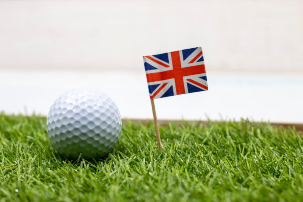 Golf ball on green grass with a small UK flag next to it