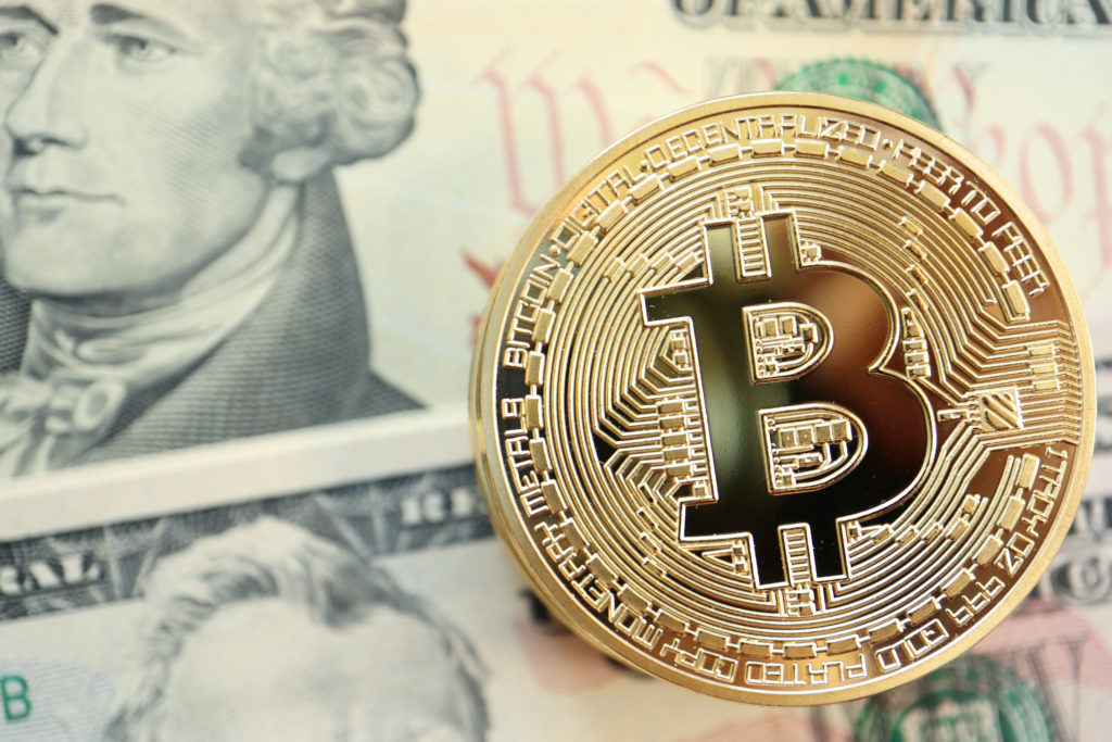 Bitcoin lying on top of a US dollar bill.