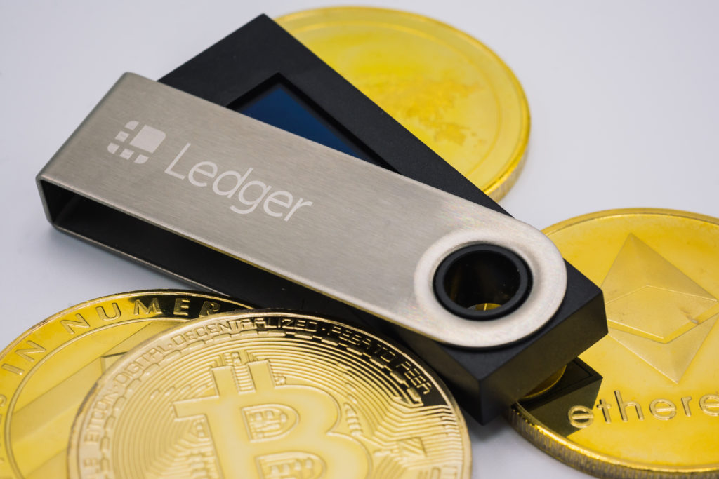 A Ledger hardware wallet lying on top of physical Bitcoin, Ethereum and other cryptocurrency coins.