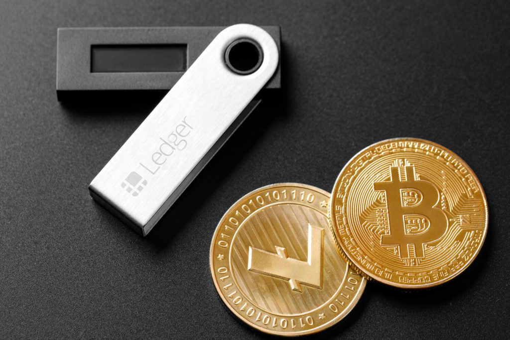 A Ledger hardware wallet sitting next to a golden Bitcoin