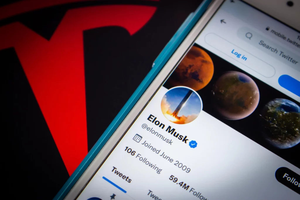 An image of Elon Musk’s Twitter account in front of the logo for Tesla
