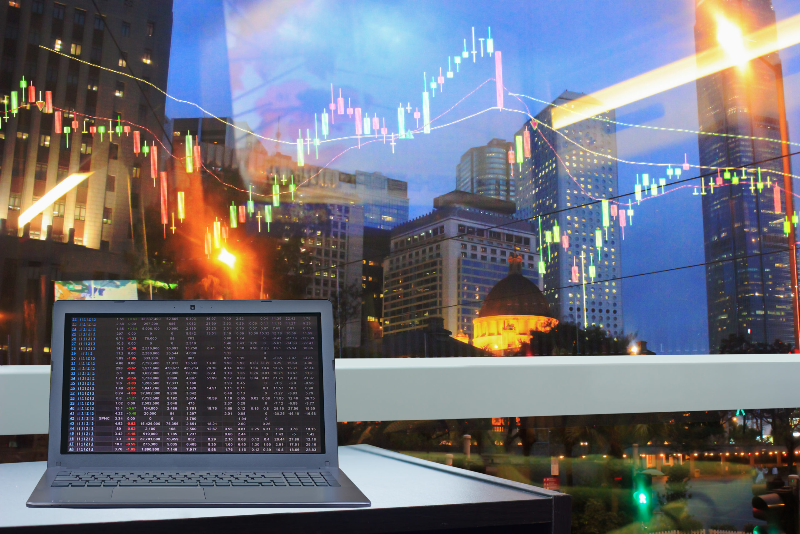 Laptop sitting on a table with graph in background imposed on a city landscape