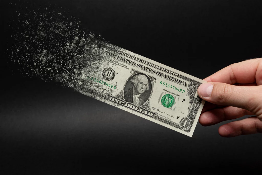 Image of a person holding a US dollar that is disintegrating at one end