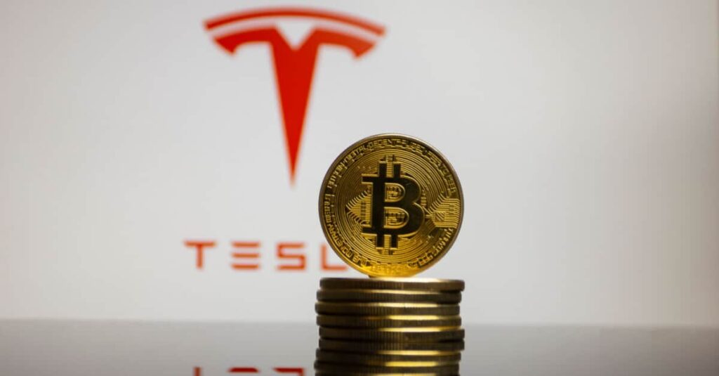Stack of golden bitcoin coins in front of the Tesla logo
