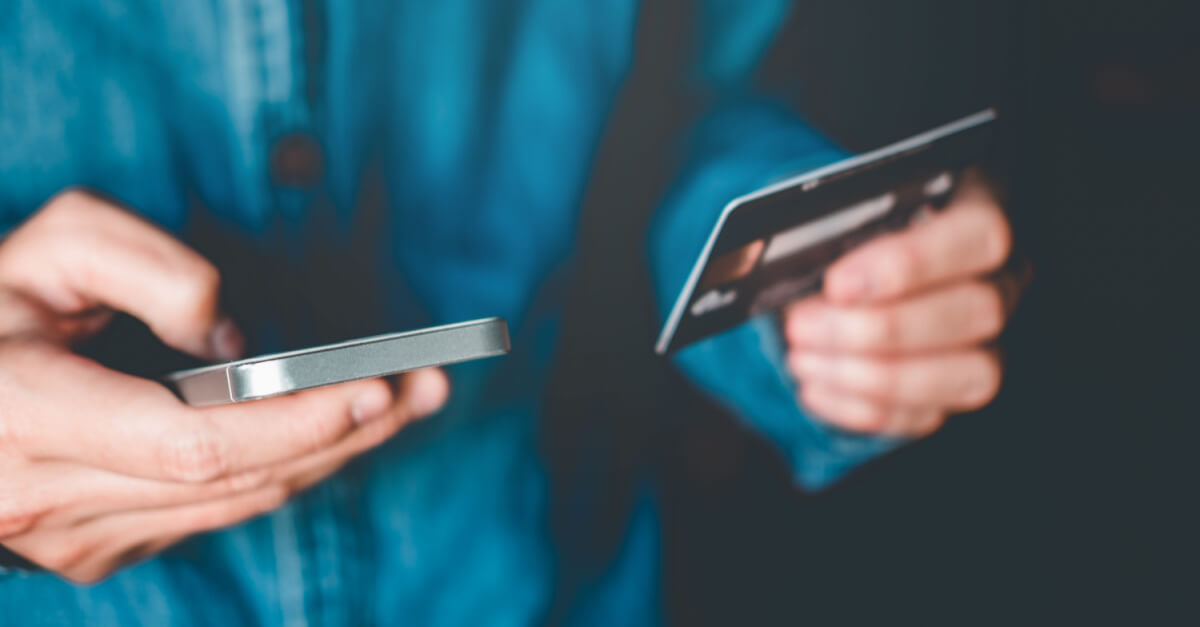 Phone and credit card being held in hands of man with blue shirt