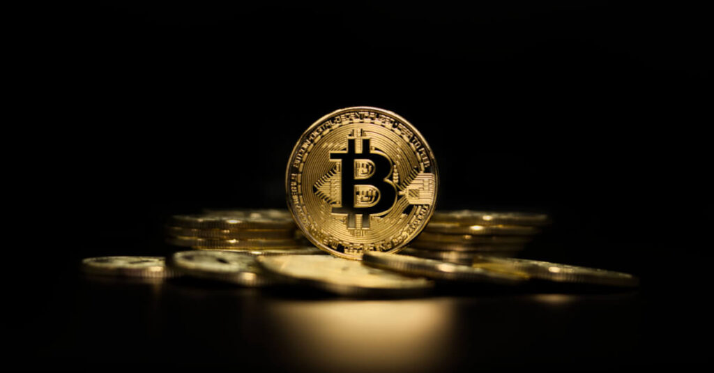 gold bitcoin standing before piled coins on black background

