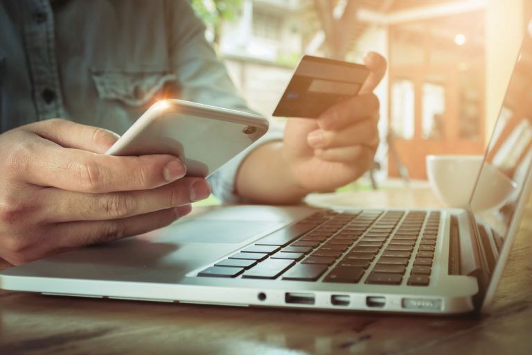 a person buying bitcoin with credit card in front of a laptop while holding phone in other hand